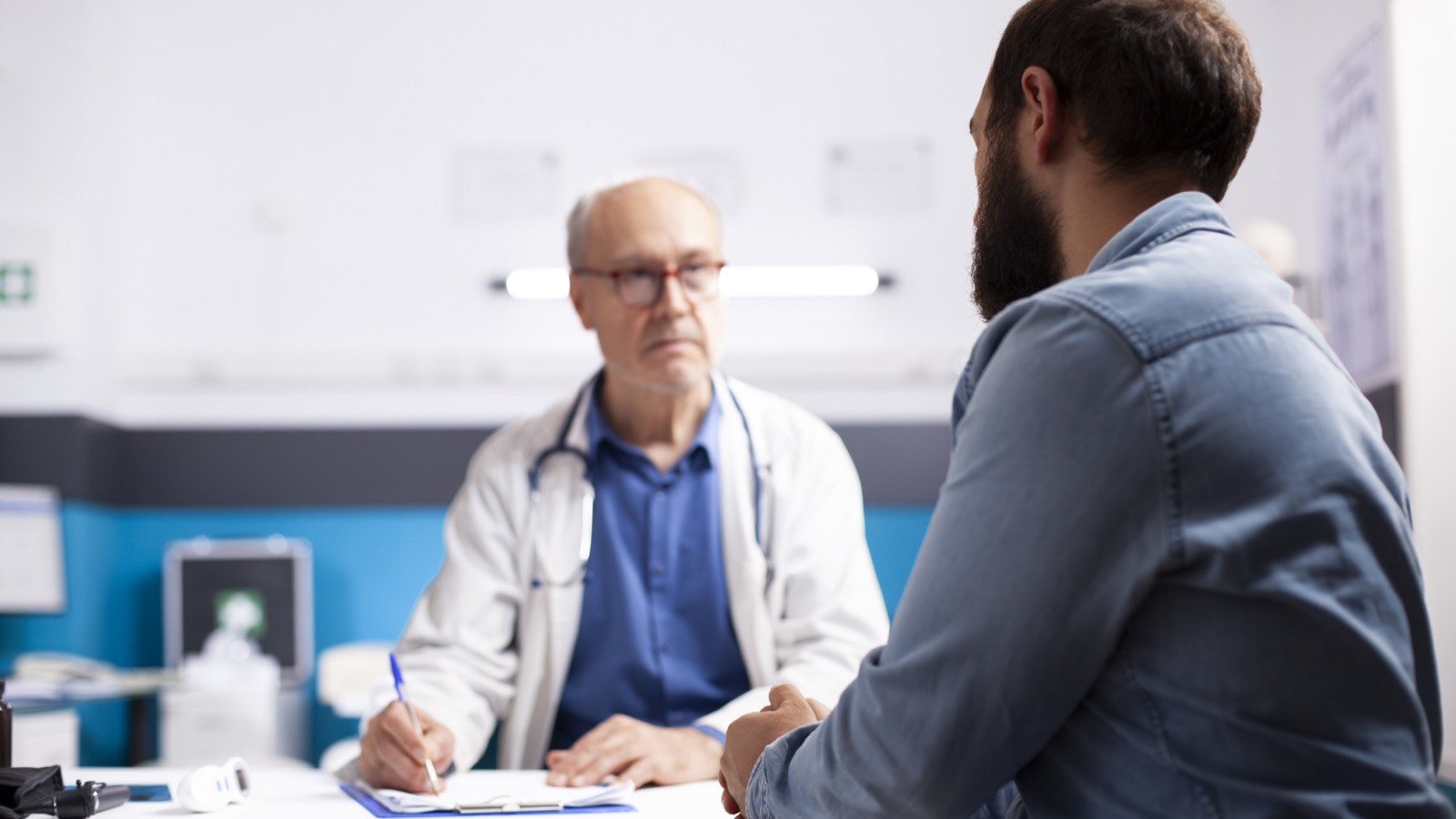 Médico à mesa do consultório conversa com um profissional de camisa jeans sobre quem vai cuidar do marketing
