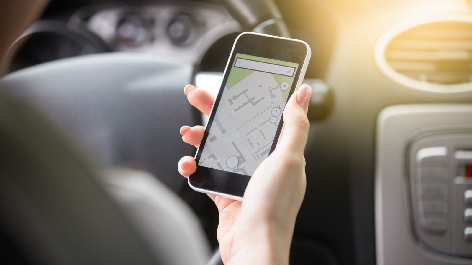 Mão segurando o celular com o mapa aberto na tela, dentro do carro, procurando o caminho até o consultório